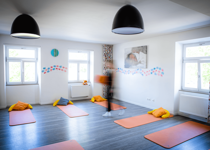 Matten auf dem Boden mit Kissen darauf, Person geht mit Matte durch den Raum