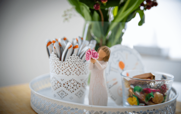 Tablett mit Blumenstrauß, Becher mit Kugelschreibern, Dekofigur, Süßigkeiten und Scheibe