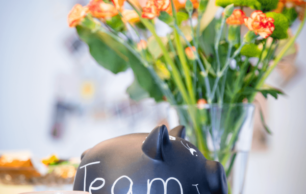 Sparschwein mit der Aufschrift Team, daneben eine Kerze und Blumenstrauß